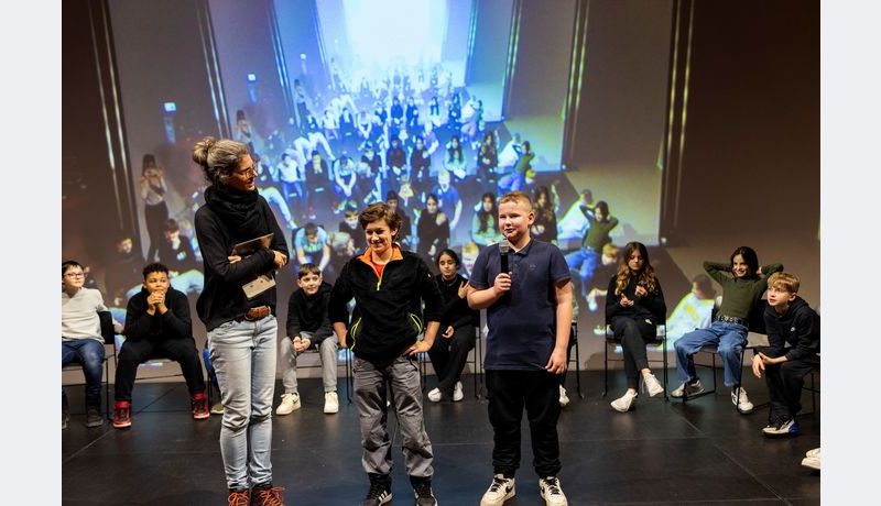 Two students stand in front of the rest of the students and speak.