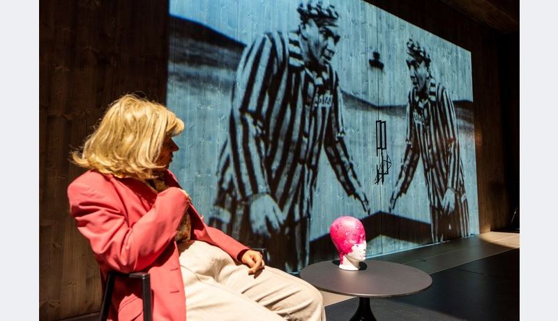Actress sits, next to her is a projection of two men in concentration camp